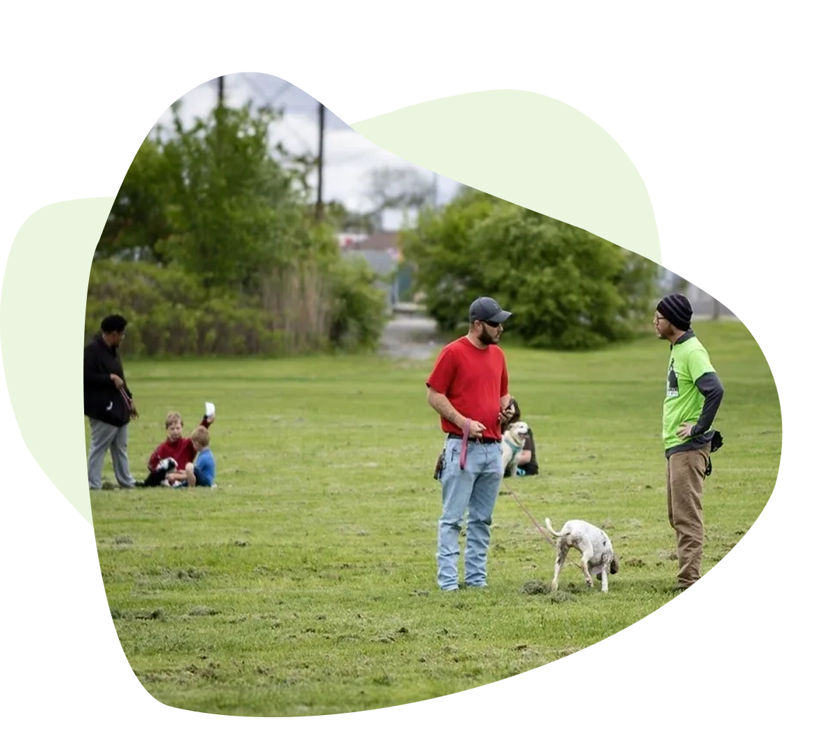 Two people standing with a dog in a grass field; others sitting in the background. Two people standing with a dog in a grass field; others sitting in the background.