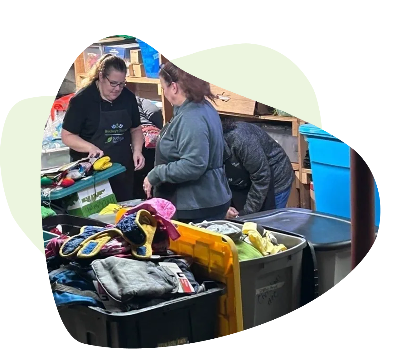 Three people sorting clothes in a room filled with bins containing various garments and items. Three people sorting clothes in a room filled with bins containing various garments and items.