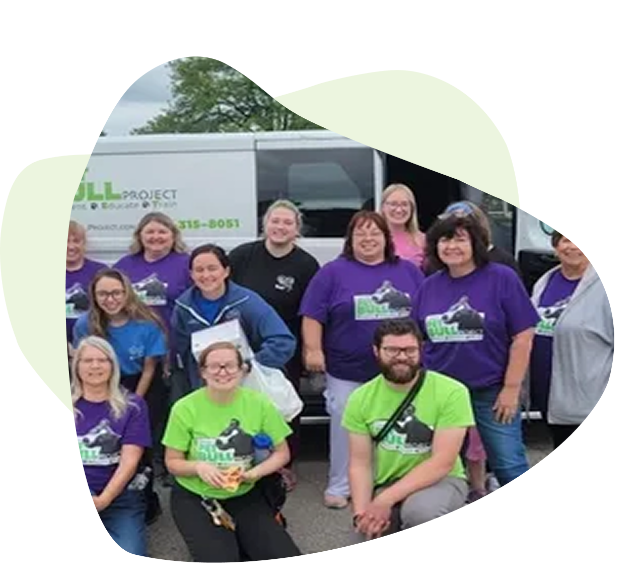 A group of people posing in front of a vehicle, wearing purple and green t-shirts with a bull graphic. A group of people posing in front of a vehicle, wearing purple and green t-shirts with a bull graphic.