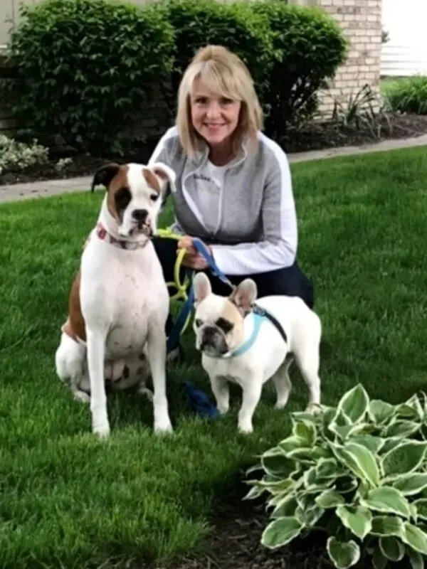 nancy A woman sitting on the grass with two dogs.