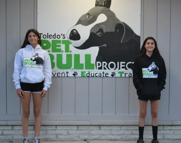 Two girls standing in front of a sign that says toledo 's pet bull project.