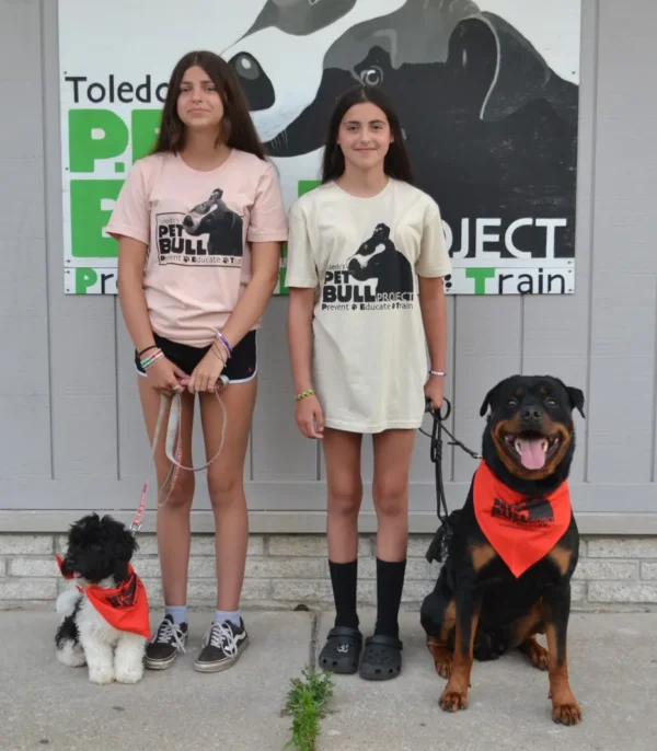 Two girls and a dog are posing for the camera.